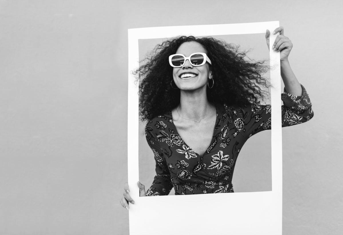 Young woman holding a large picture frame in front of a yellow background