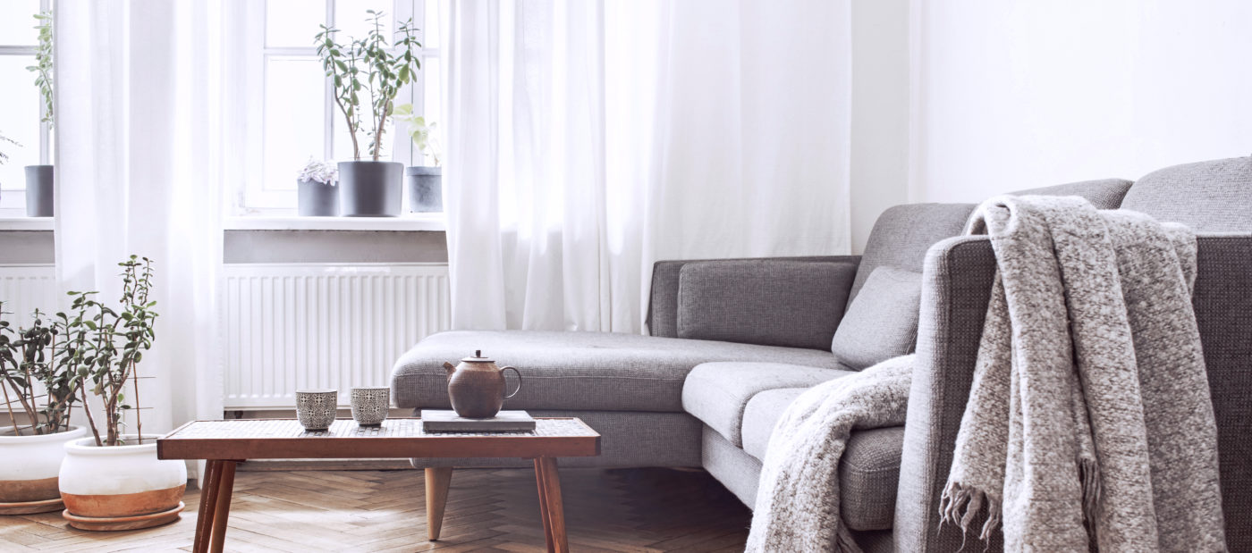 Stylish scandinavian interior of living room with small design table and sofa. White walls, plants on the windowsill. Brown wooden parquet.