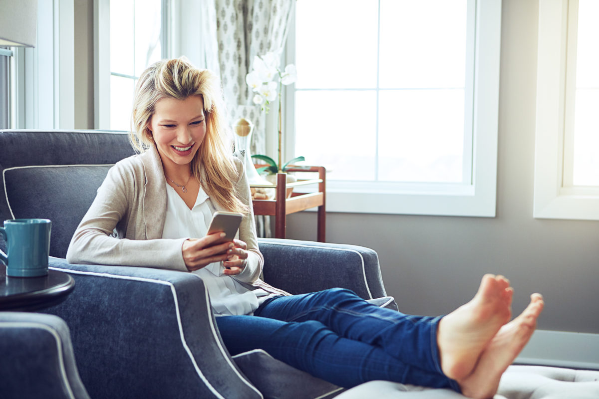 Woman using a phone while sitting on living room furniture.