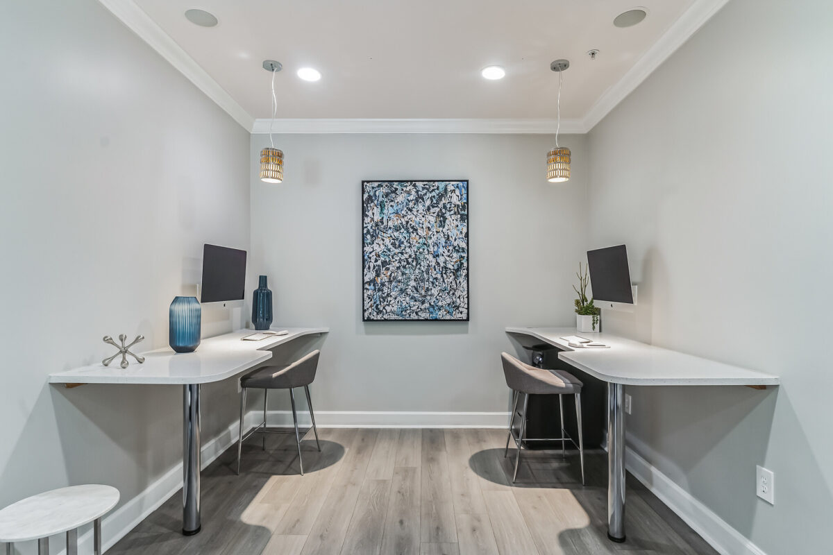 Work area with wall art, suspended lights, two tables with office chairs and computers